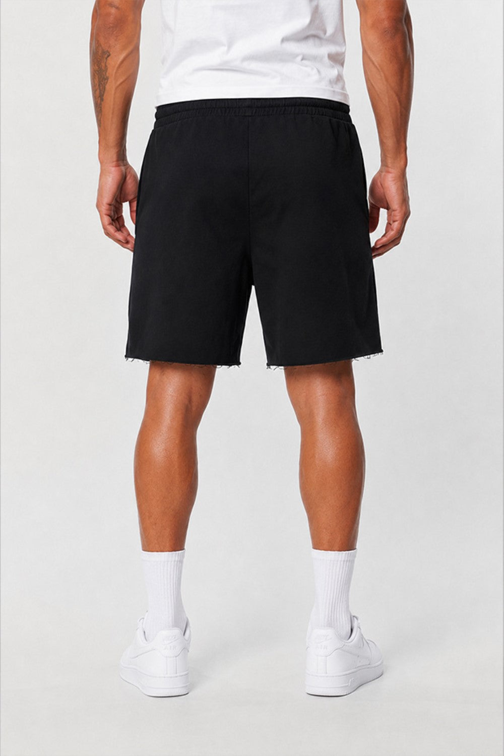 A person shown from the waist down wearing black shorts, white crew socks, and white sneakers against a light gray studio background.