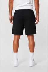 A person shown from the waist down wearing black shorts, white crew socks, and white sneakers against a light gray studio background.