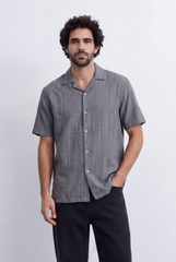 Man wearing a grey short-sleeve resort collar shirt with textured stripes and black trousers.