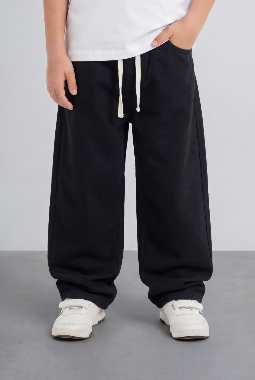 Boy's relaxed black jogger jeans in washed fabric with a drawstring waist and white sneakers.