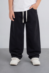 Boy's relaxed black jogger jeans in washed fabric with a drawstring waist and white sneakers.
