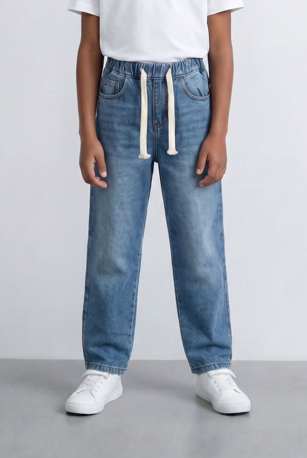Boy wearing blue drawstring denim jeans with an elastic waist and white sneakers.