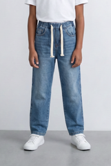 Boy wearing blue drawstring denim jeans with an elastic waist and white sneakers.