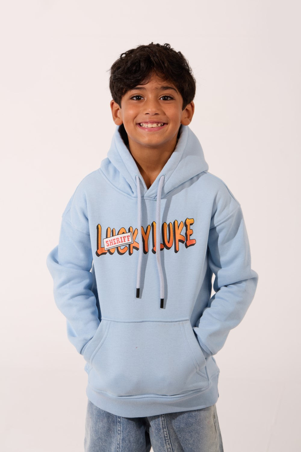 Boy wearing a light blue oversized hoodie with 'Lucky Luke Sheriff' graphic print.