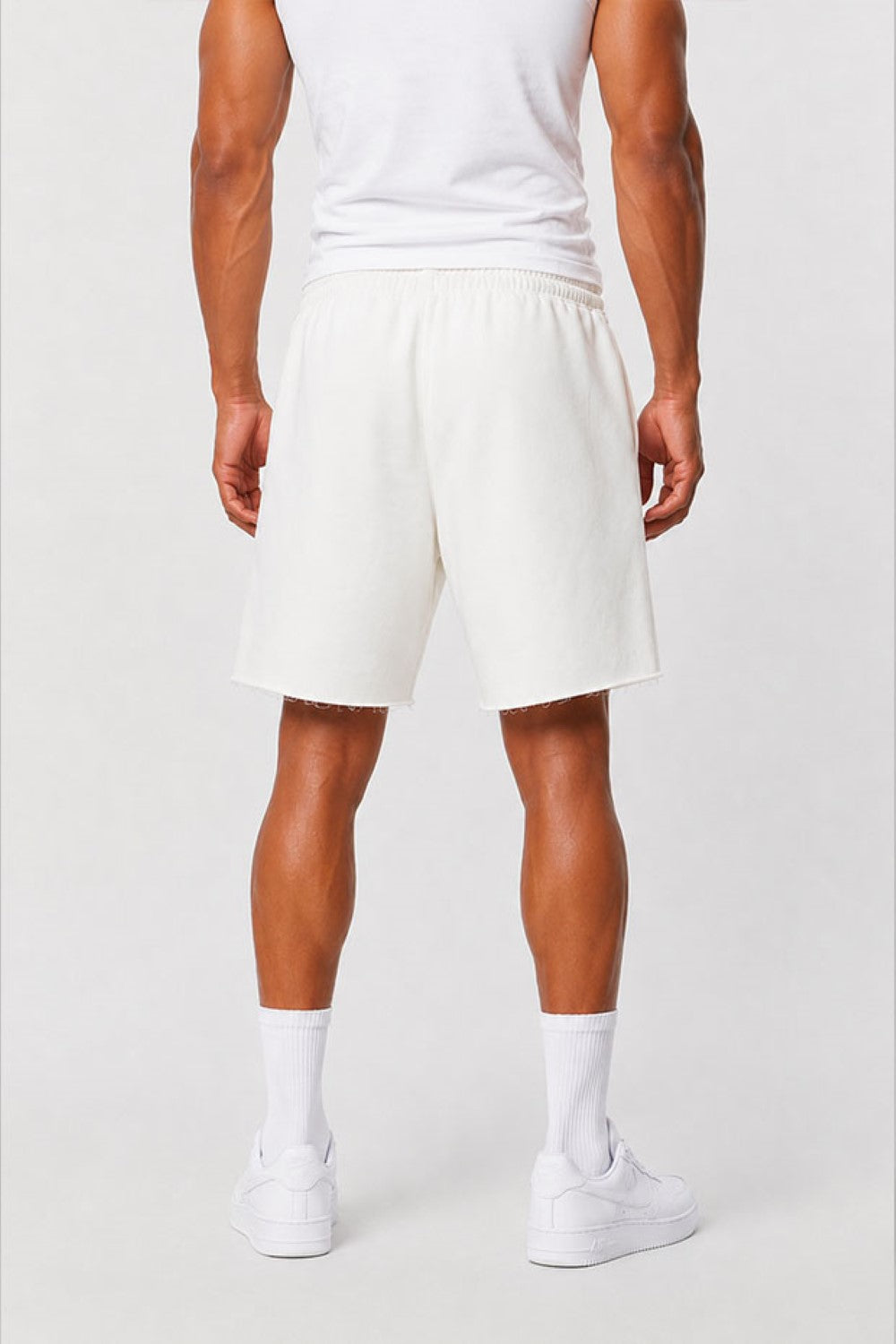 A man wearing off-white athletic shorts, a white tank top, white socks, and white sneakers, shown from the back against a light gray studio background.