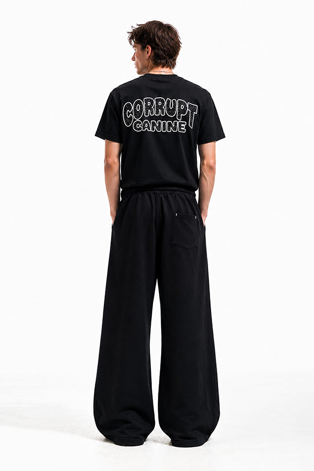 Man wearing black t-shirt with "CORRUPT CANINE" graphic and wide-leg black sweatpants.