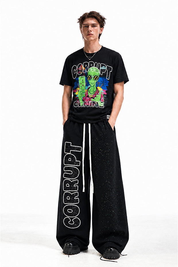 Man wearing black wide-leg sweatpants with "CORRUPT" graphic and a graphic t-shirt.