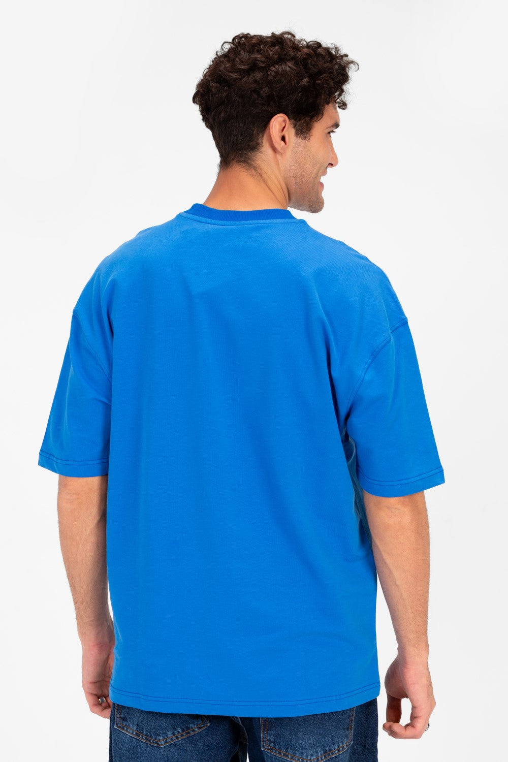 Back view of a man wearing a blue oversized t-shirt with vintage college artwork.