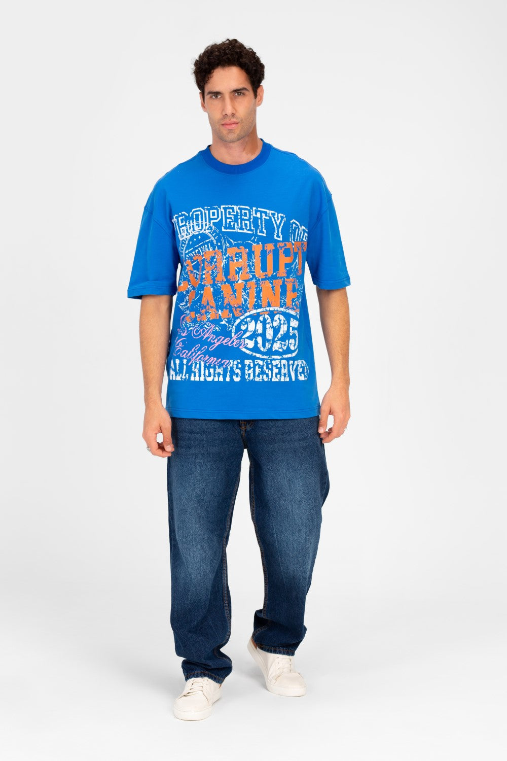 Man wearing a blue oversized t-shirt with vintage college graphic artwork and dark wash jeans.