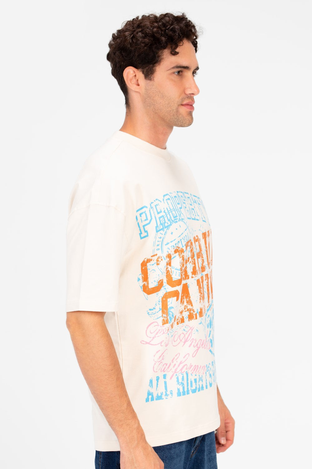Man wearing an oversized cream t-shirt with vintage college graphic artwork in blue, orange, and pink.