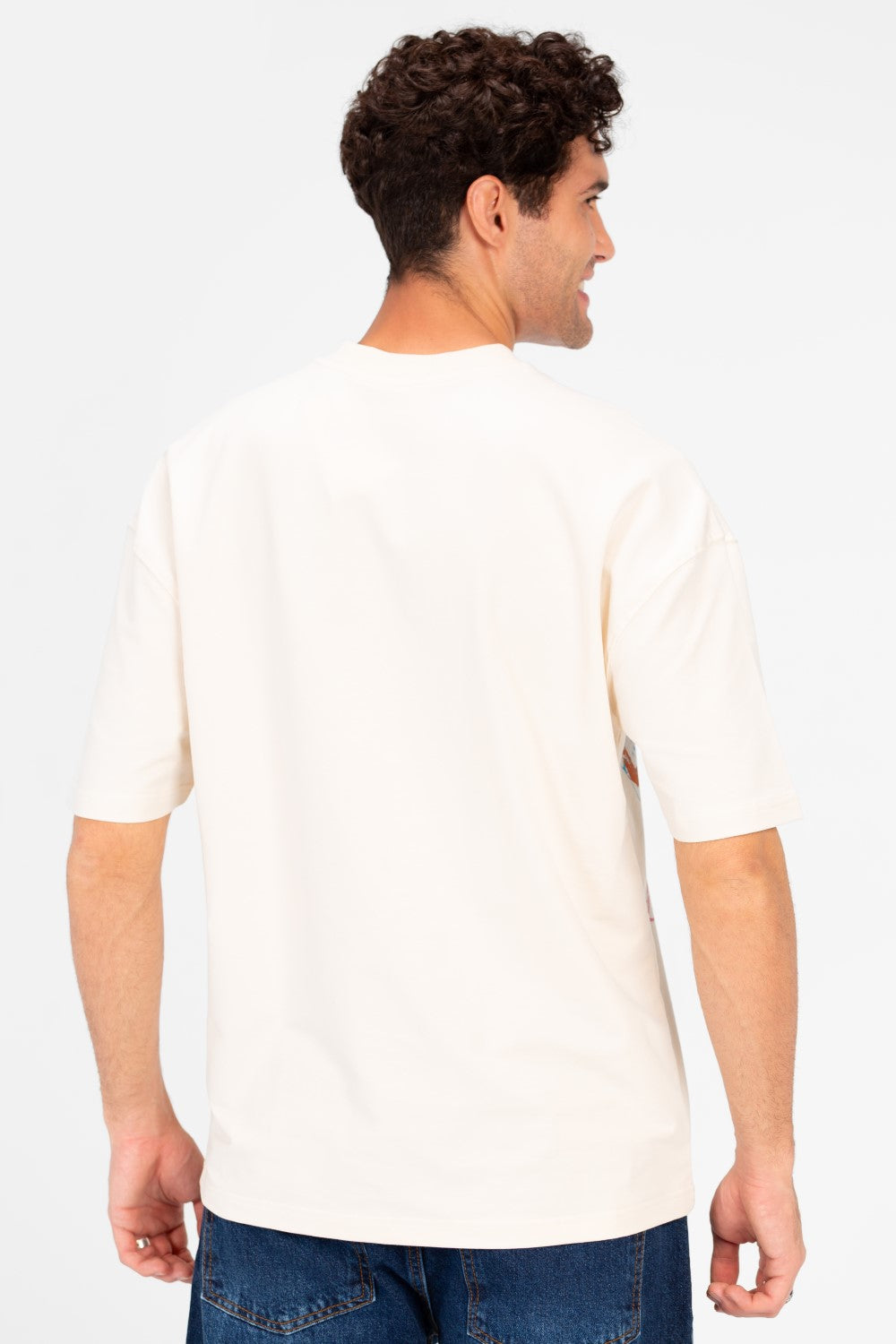 Man wearing a cream oversized t-shirt with vintage college artwork on the back.