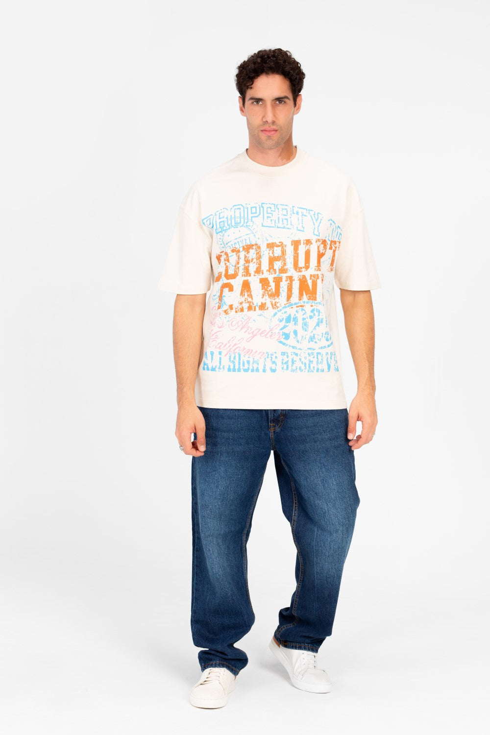 Man wearing an oversized cream t-shirt with vintage college graphic artwork and blue jeans.