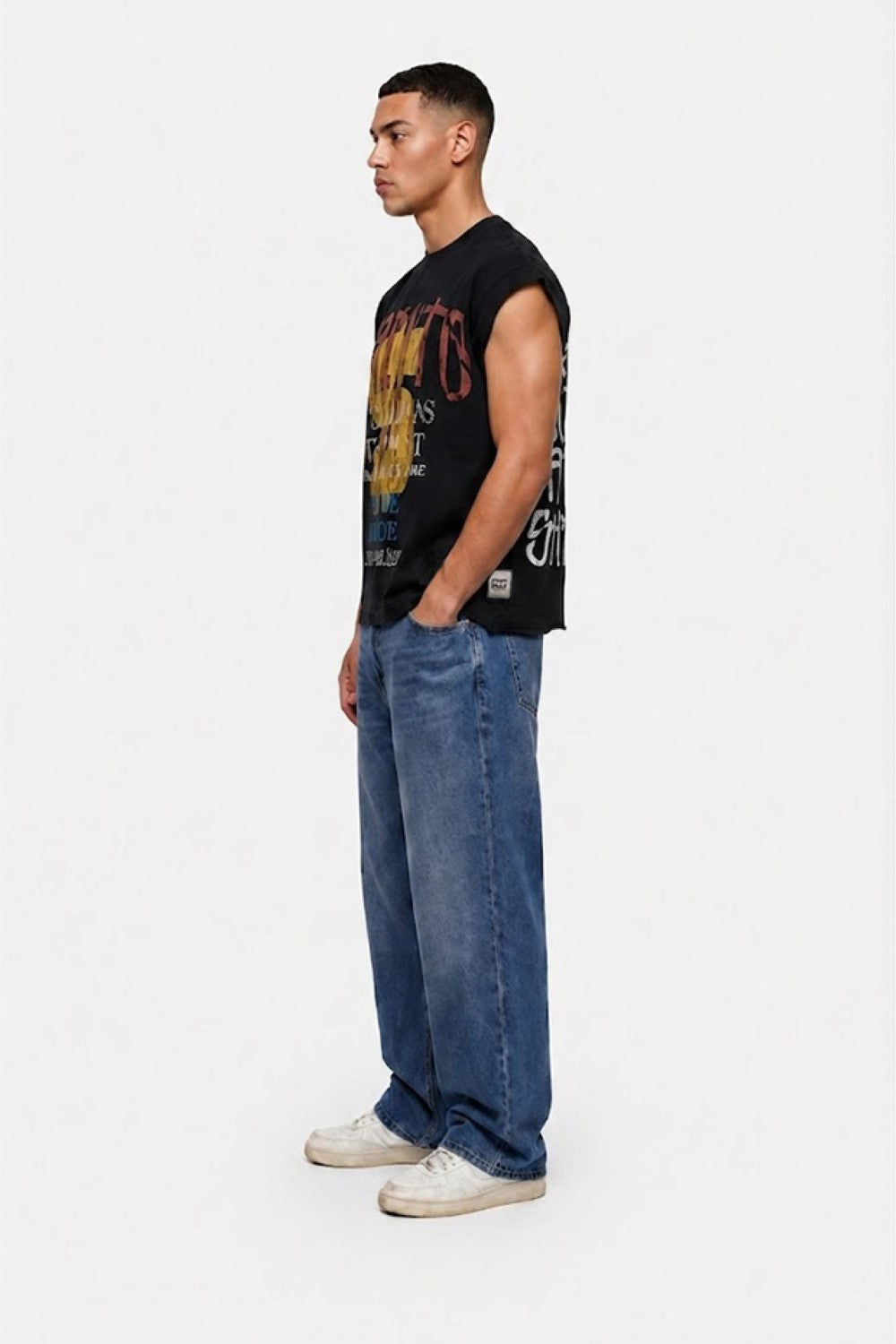 Man wearing a black graphic t-shirt, blue jeans, and white sneakers on a white background