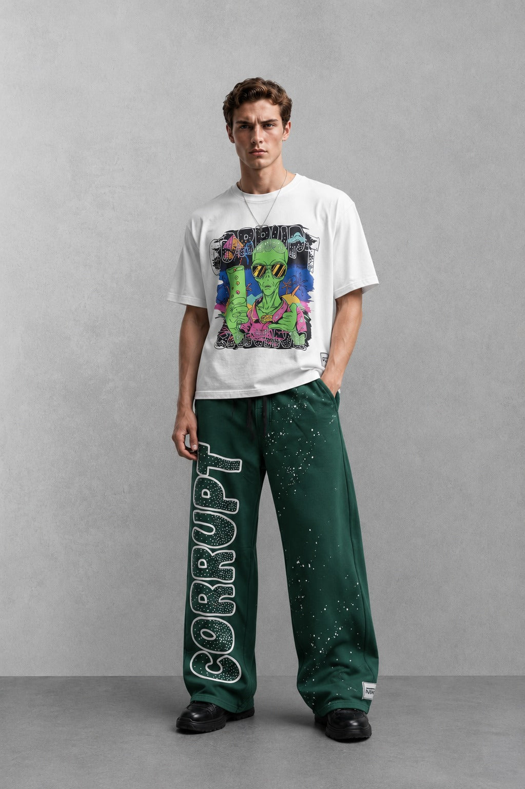 Man wearing a white graphic t-shirt with an alien design and green sweatpants with "CORRUPT" printed on the leg.