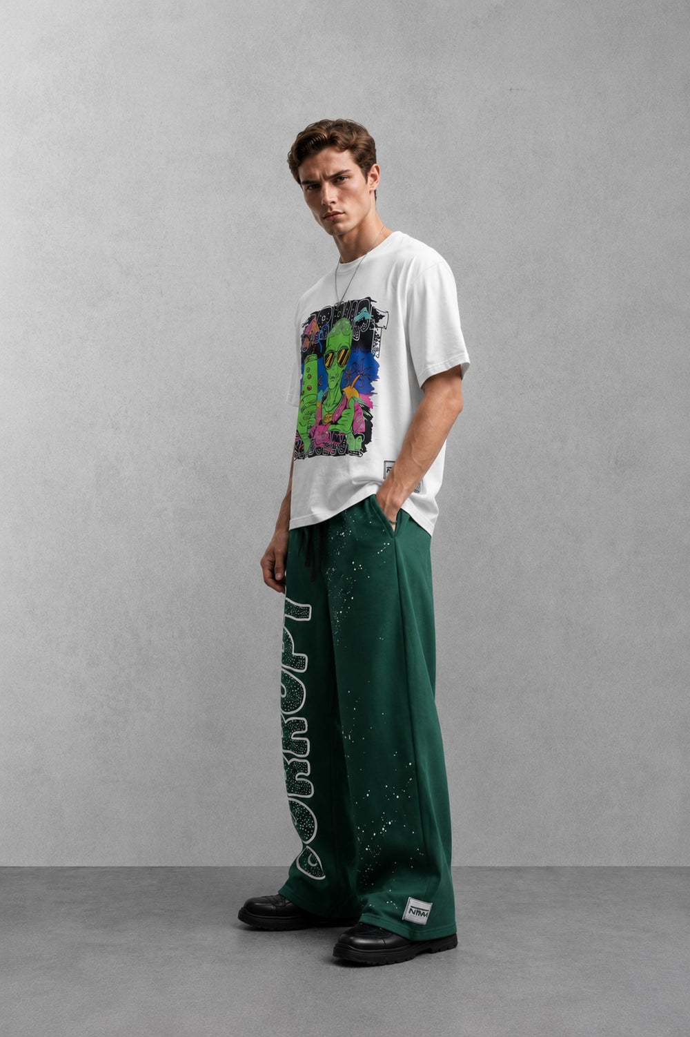 Man wearing a white graphic t-shirt with an alien design and green sweatpants with white paint splatters.